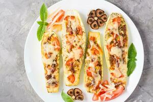 Ready-to-eat baked zucchini halves stuffed with cheese and tomato and basil leaves on a plate on the table. Vegetable dishes, healthy food. Top view. Close-up photo