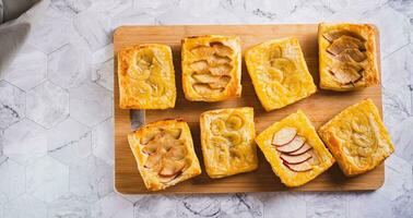 Small upside-down puff pastry cakes with banana and apple on a board top view web banner photo