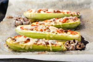 Ready-to-eat baked zucchini halves stuffed with cheese and tomato on baking paper on a baking sheet. Vegetable dishes, healthy food. Close-up photo