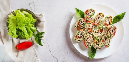 Rolled up sandwiches with lettuce, bacon and baked peppers in a tortilla top view web banner photo