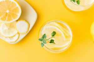 Sparkling water with lemon, melissa and ice in glasses and lemon slices on a saucer on a yellow background. Alcoholic drink hard seltzer. Close-up and top view photo