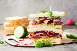 Double sandwich with pastrami, cucumber, radish and basil on a cutting board. American snack. Rustic style photo