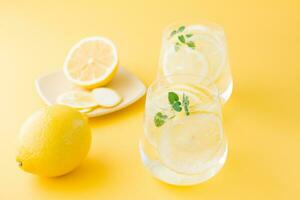 Sparkling water with lemon, melissa and ice in glasses and lemon slices on a saucer on a yellow background. Alcoholic drink hard seltzer photo