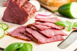 Fresh sliced marbled beef pastrami and vegetables on a cutting board. American delicacy. Rustic style. Close-up photo