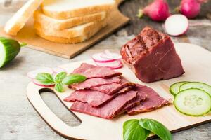 Fresh sliced marbled beef pastrami and vegetables on a cutting board. American delicacy. Rustic style photo