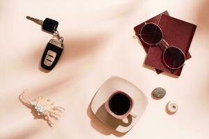 Preparing for a car trip. Passports, sunglasses, car keys, seashells and a cup of coffee on a pink background in the shadows from tree leaves. Local tourism. Top view photo