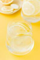 Sparkling water with lemon and ice in glasses on a yellow background. Detox drink. Vertical view photo