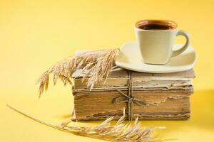 A cup of coffee on old books and dry ears of corn in yellow. Wellness, harmony, quiet reading photo