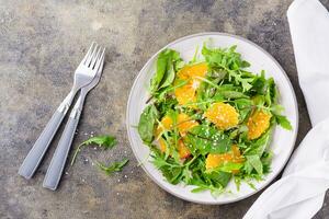 Diet vegetarian vitamin salad of orange pieces and mix of arugula, chard and mizun leaves on a plate on the table. Top view photo