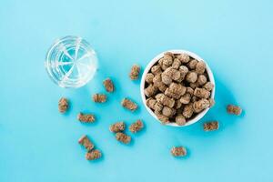 Rye bran in a bowl and on the table and a glass of water on a blue background. Diet and cleansing the body with fiber. Top view photo