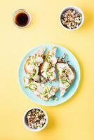 Ready-to-eat bruschetta with curd cheese, vegetables and sprouted grains on a plate on a yellow background. Healthy snacks. Top and vertical view photo