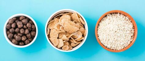 Bowls with different types of breakfasts oatmeal, cereal and chocolate balls on a light blue background. Top view. Web banner photo