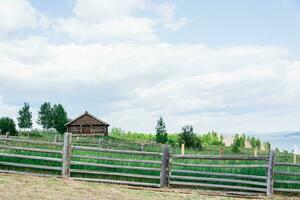 Lonely wooden old house behind a fence among lush grass on the river bank on a summer day photo