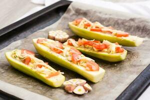 Raw zucchini halves, ready to bake, stuffed with cheese and tomato on baking paper on a baking sheet. Vegetable dishes, healthy food photo