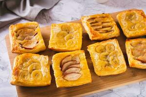 Small upside-down puff pastry cakes with banana and apple on a board photo