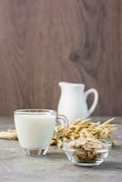 Oat milk in a cup, oatmeal and ears of corn on the table. Alternative to cow's milk. Vertical view photo