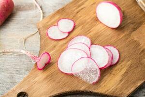 Fresh sliced radish on a cutting board on a wooden table. Vegetables for a vegetarian diet. Rustic style. Top view photo