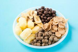 un plato con diferente tipos de desayunos y meriendas avena, cereal, chocolate pelotas, plátano papas fritas y centeno salvado en un azul antecedentes foto