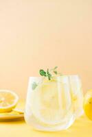 Sparkling water with lemon, melissa and ice in glasses and lemon slices on a saucer on a yellow background. Alcoholic drink hard seltzer. Close-up. Vertical view photo