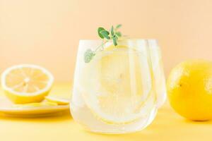Sparkling water with lemon, melissa and ice in glasses and lemon slices on a saucer on a yellow background. Alcoholic drink hard seltzer. Close-up photo