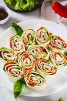 Rolled up sandwiches with lettuce, bacon and baked peppers in a tortilla on a plate vertical view photo