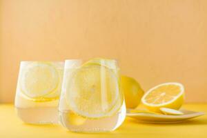 espumoso agua con limón y hielo en lentes en un amarillo antecedentes. desintoxicación bebida foto