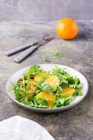 Diet vegetarian vitamin salad of orange pieces and mix of arugula, chard and mizun leaves on a plate on the table. Vertical view photo