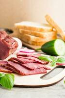 Fresh sliced marbled beef pastrami, cucumber, radish and basil on a cutting board. American delicacy. Rustic style. Vertical view photo