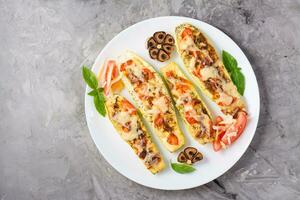 Ready-to-eat baked zucchini halves stuffed with cheese and tomato and basil leaves on a plate on the table. Vegetable dishes, healthy food. Top view. Copy space photo