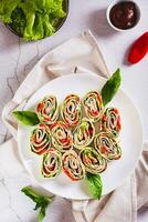 Rolled up sandwiches with lettuce, bacon and baked peppers in a tortilla top and vertical view photo