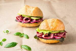 Ready-to-eat hamburgers with pastrami, cucumber, radish and herb on craft paper. American fast food photo