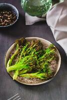 Roasted fresh broccoli sprouts in oil on a plate on the table vertical view photo