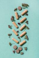 Medicinal capsules, pills and herbs in the form of a branch on a green background. Alternative medicine. Top and vertical view photo