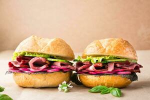 A couple of fresh burgers with pastrami, cucumber, radish and herbs on craft paper. American fast food. Copy space photo
