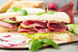 Fresh sandwiches with pastrami, cucumber, radish and basil on a cutting board. American snack. Rustic style. Close-up photo