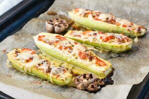 Ready-to-eat baked zucchini halves stuffed with cheese and tomato on baking paper on a baking sheet. Vegetable dishes, healthy food photo