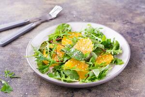 dieta vegetariano vitamina ensalada de naranja piezas y mezcla de Rúcula, acelga y mizun hojas en un plato en el mesa foto