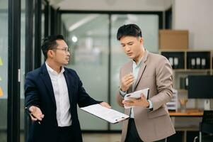 Two Asian businessman and man discuss investment project working and planning strategy with tablet laptop computer in modern office. photo