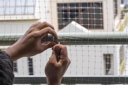 technician worker man install plastic net for protect pigeon bird in balcony apartment by hand use cable ties . Professional service man setup netting birds for clean and hygiene. photo