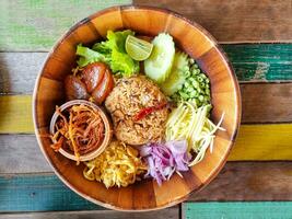 shrimp paste fried rice or kapi fried rice local thailand street food decoration with vegetable herb omelet onion cucumber in wooden plate. photo