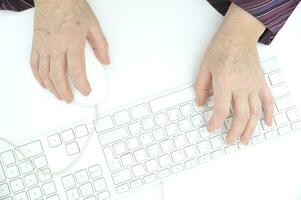 manos de un antiguo hembra mecanografía en el teclado y utilizando ratón, aislado en blanco, de cerca. foto