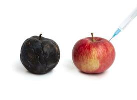 A hand with a syringe injected into a red apple photo