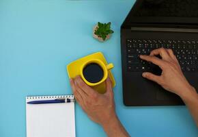 cropped shot of man typing with laptop at workplace on blue surface for mockup. Free space for text. photo