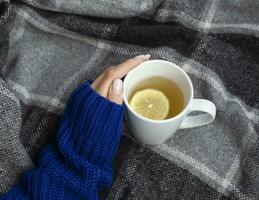 Woman's hand holding cup of tea with lemon on a cold day photo