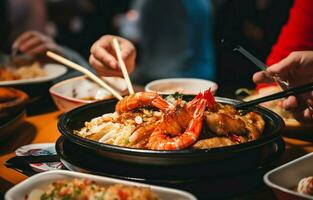 Close-up shot of hands holding chopsticks eating pork pan and seafood dishes. photo