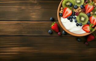 Bowl of homemade granola topped with honey, yogurt, and fresh berries including strawberries, blueberries, kiwis, and bananas on a wooden table. Shot from above, flat lay view. photo