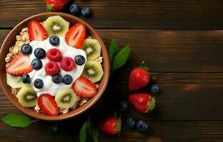 Bowl of homemade granola topped with honey, yogurt, and fresh berries including strawberries, blueberries, kiwis, and bananas on a wooden table. Shot from above, flat lay view. photo