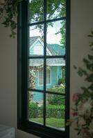 Beautiful view of the cozy house surrounded by green trees and a blue sky with clouds in the background from the window. photo