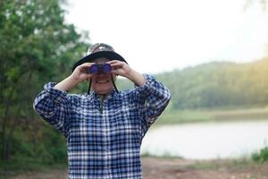 asiático mujer viajero va de viaje solo , utilizar binocular a encuesta naturaleza a el concepto de lago, de viaje, naturaleza exploración. ecología estudiar. pasatiempo actividad, estilo de vida. explorar ambiente foto