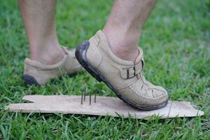 Closeup man wear shoes is stepping on rusty metal nail on wood. Concept, unsafe , risk for dangerous tetanus. Be careful and look around during walking on the floor or risk places. Accident photo